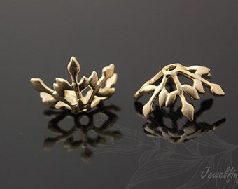 May include: Two gold-toned metal bead caps with a delicate leaf design. The caps are open at the top and bottom, allowing them to be used to cover the ends of beads or other jewelry components.