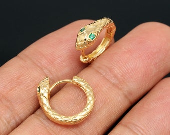 May include: A pair of gold snake hoop earrings with green gemstone accents. The earrings are textured and have a snake head design.