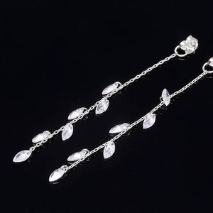 May include: A pair of silver dangle earrings with clear crystal teardrop-shaped charms hanging from a delicate chain.