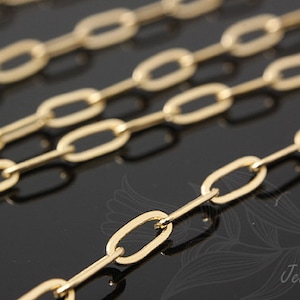 K&ouml;nnte beinhalten: Nahaufnahme einer goldenen Kette mit ovalen Gliedern. Die Kette liegt auf einer schwarzen Oberfl&auml;che.