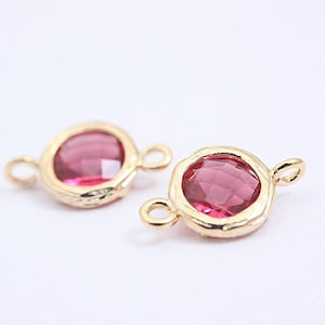 May include: Two gold-toned metal charms with a pink faceted glass stone in the centre. Each charm has a loop on the side for attaching to jewellery.