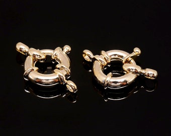 May include: Two gold-coloured toggle clasps, designed for jewellery making, are displayed against a black background. Each clasp features a circular ring with a bar that inserts into the ring to secure the clasp. The clasps are highly reflective.