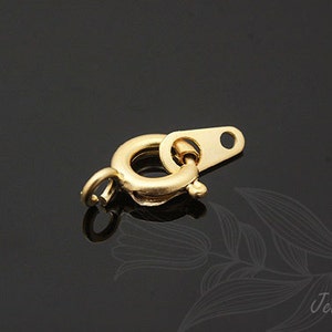 Puede incluir: Cierre de metal dorado con un anillo redondo y una pieza plana rectangular con un agujero. El cierre está diseñado para sujetar cadenas o collares de joyería.