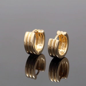 Puede incluir: Un par de pendientes de aro de oro con un diseño de triple capa. Los pendientes son simples y elegantes.