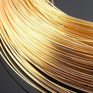 Puede incluir: Primer plano de un carrete de alambre de color dorado. El alambre está enrollado apretadamente, creando una superficie lisa y brillante.