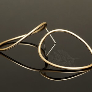 May include: A pair of gold-toned earrings with a simple, abstract design. One earring is a curved, open loop, while the other is a more rounded, oval shape.