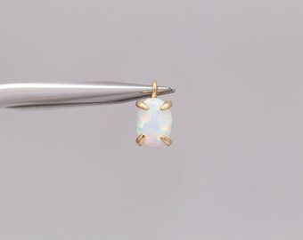 May include: A small, oval-shaped pendant with a gold-colored setting. The pendant features a white opal stone with iridescent flashes of color. The setting has four prongs that secure the stone. The pendant is suspended from a small loop.