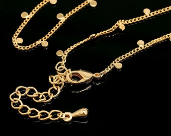 May include: A gold chain necklace with a lobster clasp and small round charms. The necklace is on a black background.
