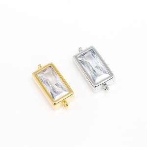 Puede incluir: Dos conectores rectangulares de cristal, uno dorado y otro plateado, con un cristal transparente en el centro. Los conectores tienen un bucle en cada extremo para sujetar a las joyas.
