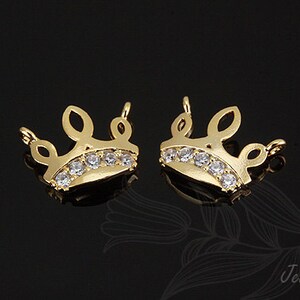 May include: Two gold-tone crown-shaped charms with clear crystal accents. The charms have a loop at the top for attaching to jewelry.