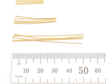 May include: Several gold-coloured head pins of different lengths are displayed against a white backdrop. A ruler with millimetre and 1/2mm markings is positioned below for scale. These pins are often used in jewellery making and various craft projects.