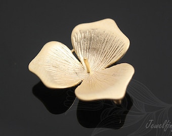 May include: A gold-coloured metal flower charm with four petals. The petals have a textured surface and a slightly raised centre.