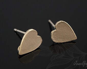 May include: A pair of gold heart-shaped stud earrings. The earrings are simple and elegant, with a smooth, matte finish.