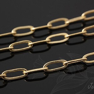 K&ouml;nnte beinhalten: Nahaufnahme einer goldenen Kette mit ovalen Gliedern. Die Kette liegt auf einer schwarzen Oberfl&auml;che.