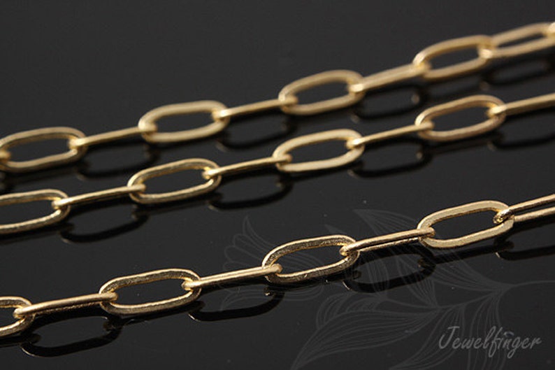 K&ouml;nnte beinhalten: Nahaufnahme einer goldenen Kette mit ovalen Gliedern. Die Kette liegt auf einer schwarzen Oberfl&auml;che.