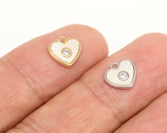 May include: Two heart-shaped charms with a white enamel finish and a clear rhinestone in the center. One charm is gold-toned and the other is silver-toned.