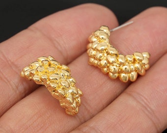 May include: A pair of gold-colored, half-hoop earrings. Each earring is studded with small, rounded, textured elements, giving them a clustered appearance. The earrings are set against a neutral background.