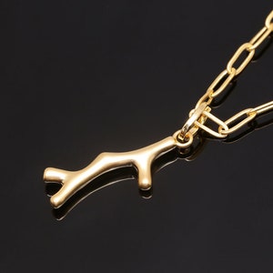 K&ouml;nnte beinhalten: Eine goldene Kettenkette mit einem goldenen Ast-Anh&auml;nger. Die Kette ist im einfachen Glieder-Stil.
