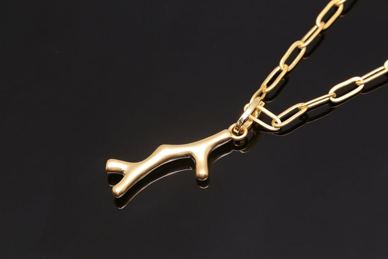 K&ouml;nnte beinhalten: Eine goldene Kettenkette mit einem goldenen Ast-Anh&auml;nger. Die Kette ist im einfachen Glieder-Stil.