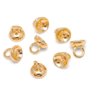 May include: Gold-coloured metal jewellery findings, including small bell-shaped components with a loop and a circular base. The findings are shown against a white background. These components are likely used in jewellery making.