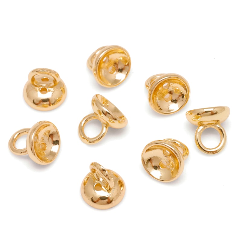 May include: Gold-coloured metal jewellery findings, including small bell-shaped components with a loop and a circular base. The findings are shown against a white background. These components are likely used in jewellery making.