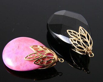 May include: Two teardrop-shaped pendants. One is pink, the other is black. Both have gold-coloured leaf-shaped caps with a small loop at the top. The pendants are displayed on a reflective black surface.