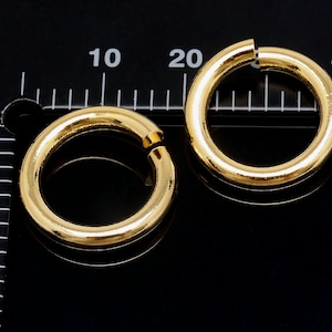May include: Two gold-coloured metal rings, one larger than the other, are shown on a black surface with a ruler in the background. The ruler is marked in inches.