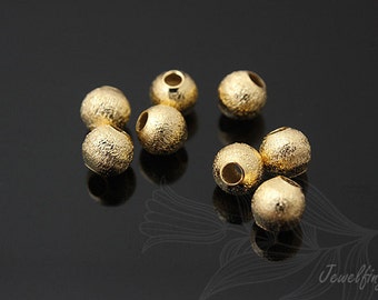 May include: A group of eight gold-colored metal beads with a textured surface. The beads are round and have a hole in the center.