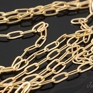 K&ouml;nnte beinhalten: Nahaufnahme einer goldenen Kette mit ovalen Gliedern. Die Kette liegt auf einer schwarzen Oberfl&auml;che.