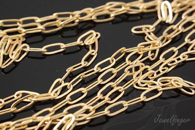 K&ouml;nnte beinhalten: Nahaufnahme einer goldenen Kette mit ovalen Gliedern. Die Kette liegt auf einer schwarzen Oberfl&auml;che.