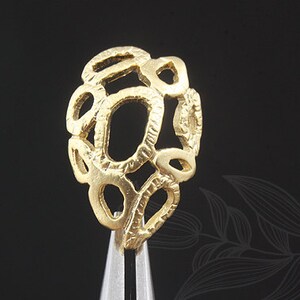 May include: A gold-coloured ring with a unique design featuring a cluster of interconnected circles and ovals. The ring is textured and has a delicate, intricate look.