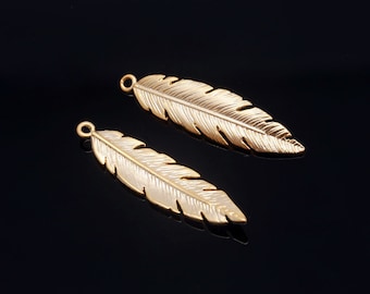 May include: Two gold-tone metal feather charms with a textured surface. The feathers are about 2 inches long.