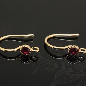 May include: A pair of gold earring hooks with a small red gemstone on each hook.