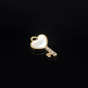 May include: A gold-tone key charm with a white heart-shaped pendant and clear rhinestones. The charm is perfect for adding a touch of whimsy to jewelry or crafts.