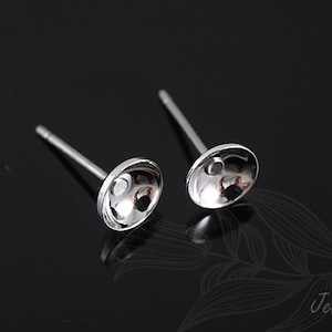 May include: A pair of silver stud earrings with a round, slightly concave top. The earrings are on a black background.