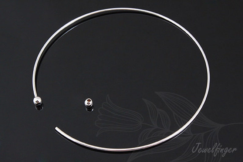 May include: A silver choker necklace with a simple, minimalist design. The necklace is made of a thin, flexible wire and has a small, round bead at each end.