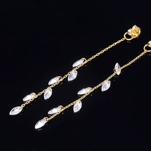 May include: A pair of gold dangle earrings with clear crystal teardrop-shaped charms hanging from a delicate chain.