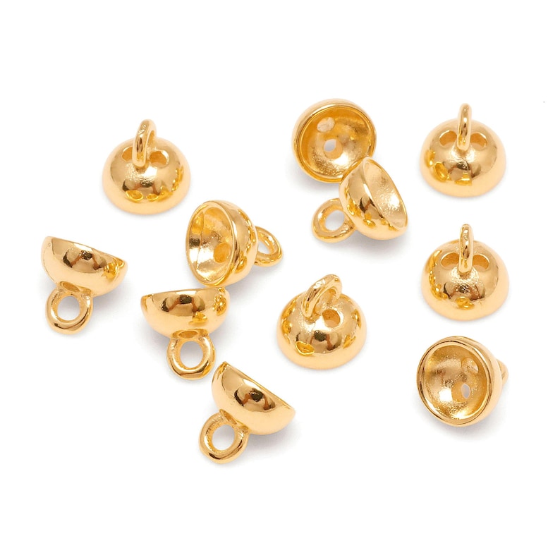 May include: A selection of gold-coloured jewellery findings, including bell-shaped beads with small loops and rounded beads with a loop on top. The beads are arranged on a white surface, showcasing their shiny, metallic finish. These findings are ideal for jewellery making.