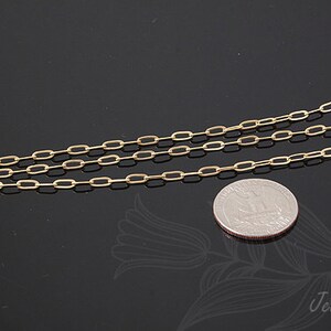 K&ouml;nnte beinhalten: Eine goldene Kettenkette mit einem zarten, ovalen Gliederdesign. Die Kette liegt auf einer schwarzen Oberfl&auml;che neben einem US-amerikanischen Viertel f&uuml;r die Skalierung.