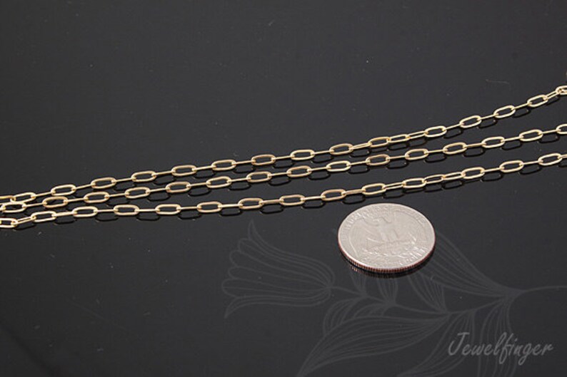 K&ouml;nnte beinhalten: Eine goldene Kettenkette mit einem zarten, ovalen Gliederdesign. Die Kette liegt auf einer schwarzen Oberfl&auml;che neben einem US-amerikanischen Viertel f&uuml;r die Skalierung.