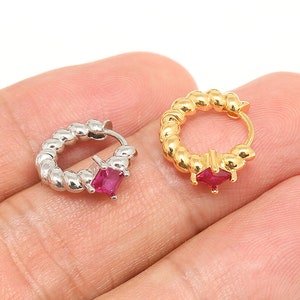 May include: Two hoop earrings with a red gemstone. One earring is silver and the other is gold.
