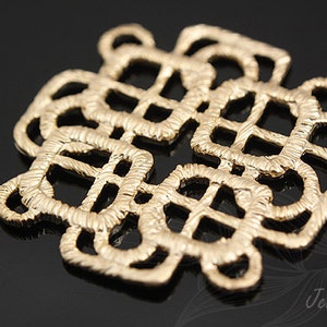 May include: A gold-colored metal pendant with a intricate knot design. The pendant is made of a woven metal and has a textured surface.