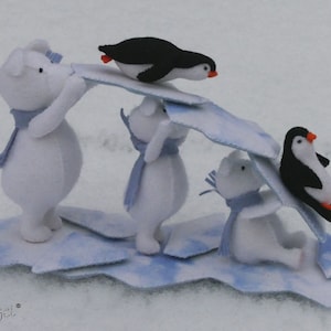 Könnte beinhalten: Eine Szene aus Filz mit Eisbären und Pinguinen auf einer Eisscholle. Die weißen Eisbären tragen blaue Schals und tragen eine blau-weiße Eisplatte. Zwei Pinguine mit schwarz-weißem Körper und orangefarbenen Füßen und Schnäbeln befinden sich auf dem Eis.