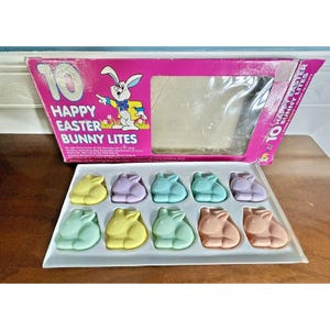 May include: A vintage box of Happy Easter Bunny Lites. The pink box features a cartoon bunny and the text "Happy Easter Bunny Lites". Inside, a tray holds ten pastel-colored bunny-shaped lights in various colors.