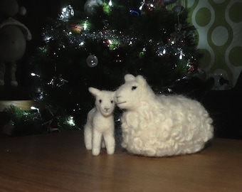 Pode incluir: Duas ovelhas brancas e felpudas feitas de feltro, uma é maior que a outra, em pé em frente a uma árvore de Natal com luzes brancas.