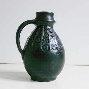 May include: A black ceramic vase with a swirling pattern. The vase has a rounded body and a handle.