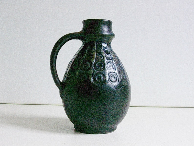 May include: A black ceramic vase with a swirling pattern. The vase has a rounded body and a handle.