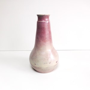 May include: A handcrafted ceramic vase with a bulbous base and a slender neck. The vase features a gradient of colors, transitioning from a deep rose at the top to a pale, speckled pink at the base. The vase is approximately 8 inches tall.