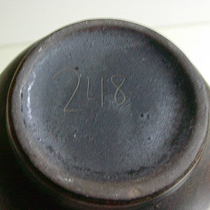 May include: A dark gray ceramic vase with the number 248 inscribed on the bottom.
