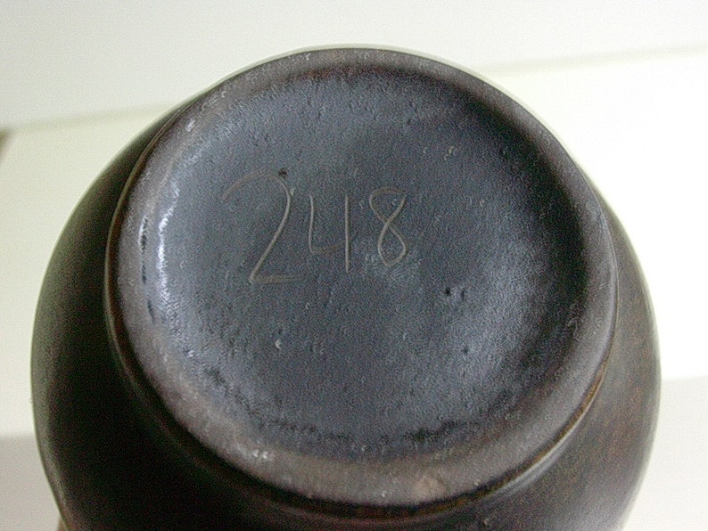 May include: A dark gray ceramic vase with the number 248 inscribed on the bottom.